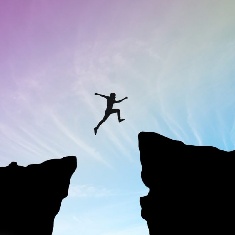 man-jump-through-gap-hill-man-jumping-cliff-sunset-background-business-concept-idea-min